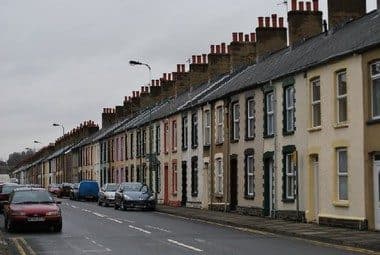 Terraced street with parked cars and lighting columns — the everyday scene a visual check has to read for clues to what is buried.