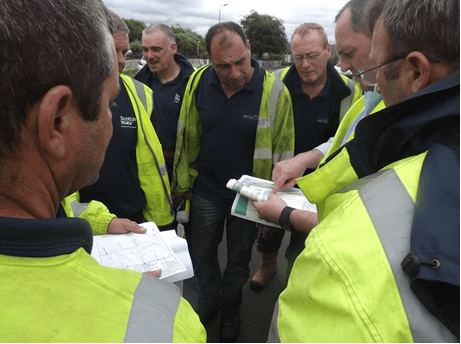 A crew in hi-vis gathered round utility plans on site.