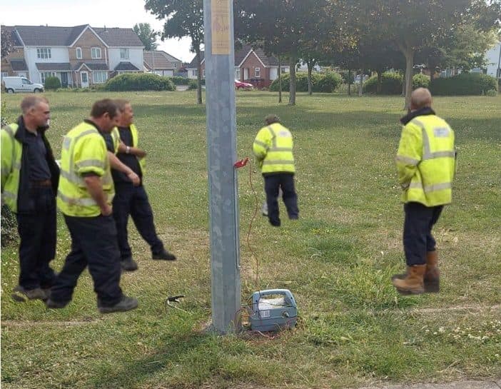 Training group watching a locate at a lighting column on open grass.