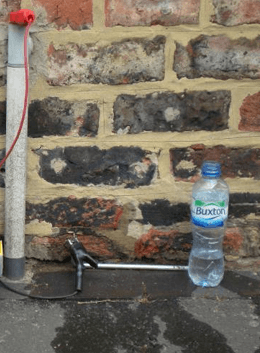 Earth pin and lead at the base of a stone wall, water bottle beside for wetting the earth.