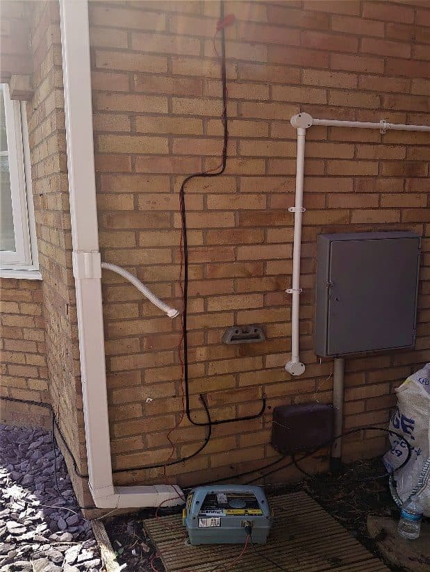 Genny at the corner of a house, meter box and downpipes on the wall above.
